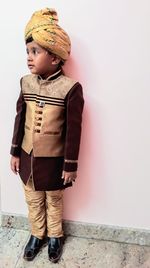 Boy in traditional clothing and turban standing against wall