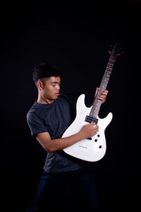 Full length of a young man playing guitar against black background