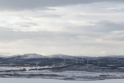 Scenic view of snow covered land with wind turbines against sky.