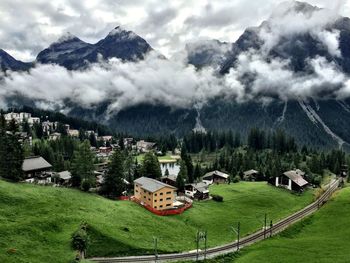 Scenic view of alps by houses against cloudy sky