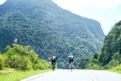 Rear view of people riding bicycle on road