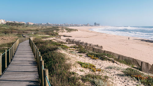 Boardwalk leading towards sea against clear sky