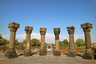 Rear view of woman standing amidst columns against blue sky