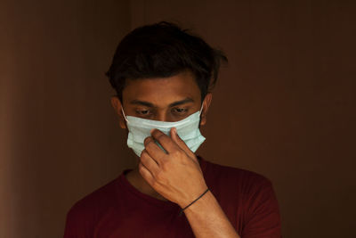 Close-up of young man wearing flu mask standing against black background