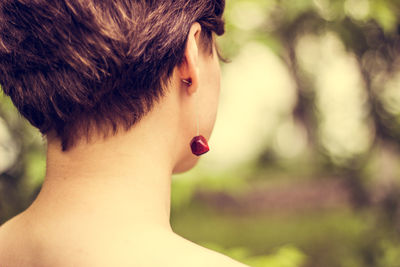 Close-up of young woman wearing red earring against plants