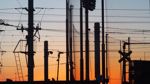 Silhouette electricity pylons against sky during sunset