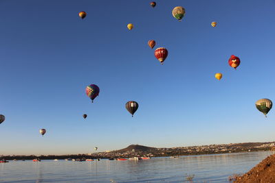 Hot air balloons flying over lake against clear sky