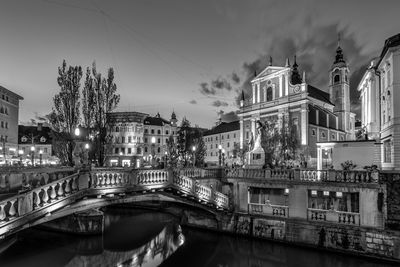 Arch bridge over river amidst buildings in city against sky