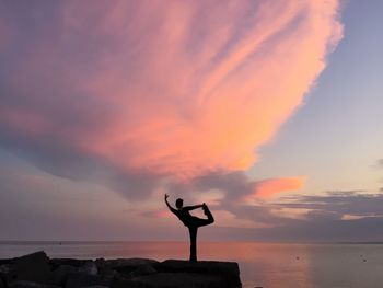 Silhouette woman doing yoga by sea against cloudy sky during sunset
