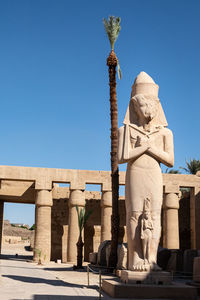 Egyptian statue with mini statue. pillars. date palm tree.