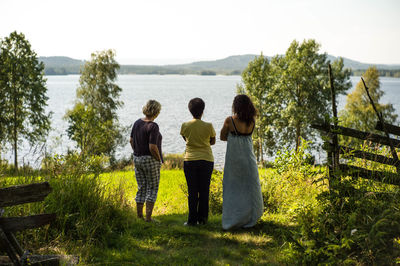 Rear view of friends standing on grassy field in front of lake