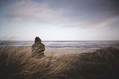 Rear view of woman sitting on beach against sky