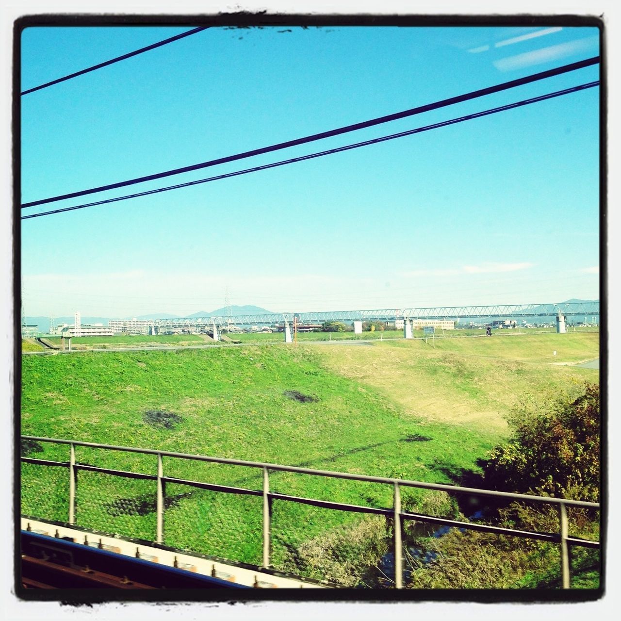 field, grass, sky, landscape, transfer print, fence, power line, electricity pylon, grassy, auto post production filter, tranquil scene, rural scene, tranquility, green color, nature, blue, connection, day, railroad track, cloud - sky