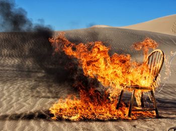 Burning chair on sand dune against clear blue sky