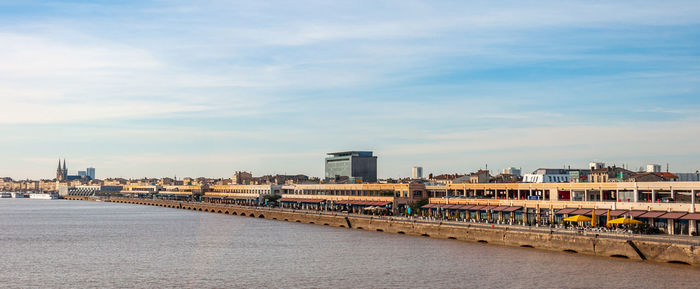 Bridge over river by buildings in city against sky