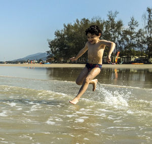 Full length of shirtless man jumping in water against sky