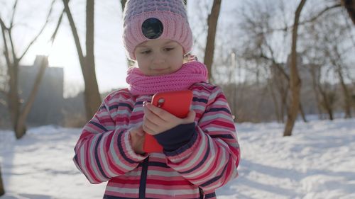 Cute girl holding smart phone during winter