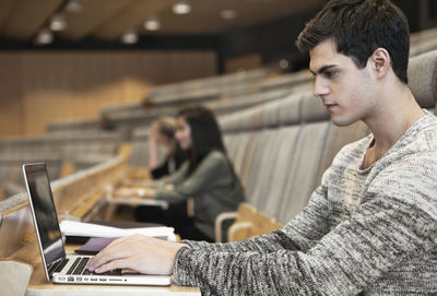 Side view of handsome young man using laptop in convention center