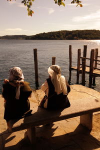 Rear view of men sitting on bench by lake