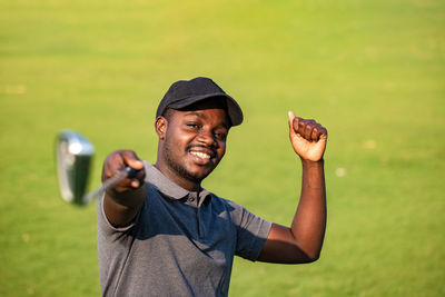 Portrait of young man wearing hat standing against grass