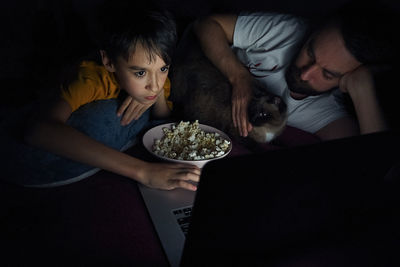 High angle view of boy with father watching movie in darkroom