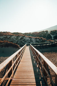 Footbridge leading towards mountains against clear sky