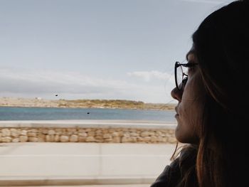 Close-up of woman looking away at beach against sky