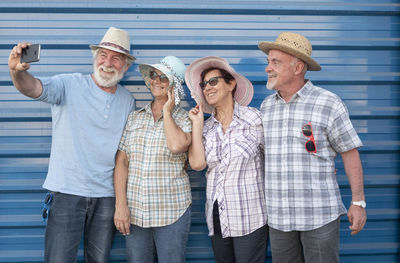 Senior man taking selfie with friends while standing against wall