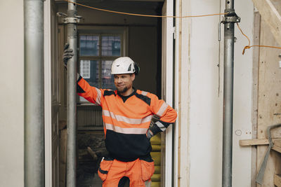 Smiling male construction worker looking away while standing with hand on hip at site