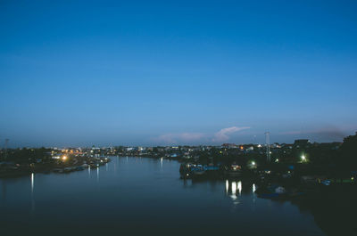 River amidst illuminated city against clear blue sky at dusk