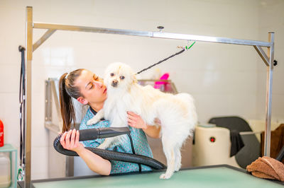 Woman groomer drying a small dog hair with a hair blower over a grooming table