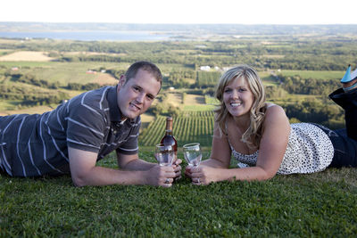 Portrait of smiling young couple lying on grass with wine bottle