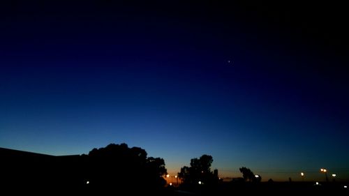 Silhouette trees against clear blue sky at night