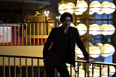 Man standing by railing against illuminated building at night