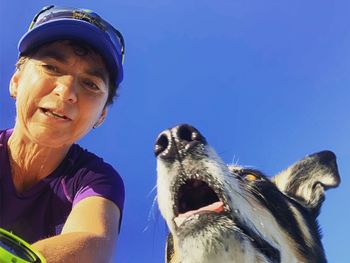 Portrait of woman with dog against blue sky