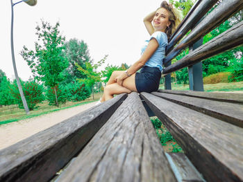 Portrait of smiling young woman sitting on wood against sky