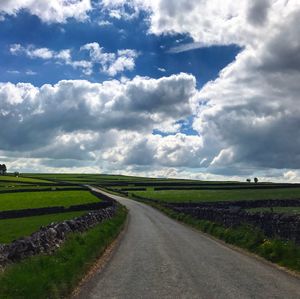 Road by agricultural field against sky