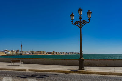 Street light by sea against clear blue sky