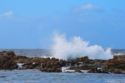 Water splashing on rocks by sea against sky