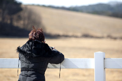 Rear view of man standing by fence at field