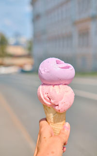 Ice cream cone in hand close-up with bokeh. gelato with strawberry and lavender flavor. 