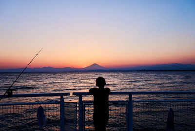 Silhouette man fishing on sea against sky during sunset