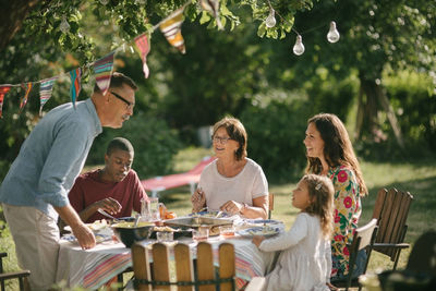 Senior man and granddaughter talking while having lunch with family in backyard during party