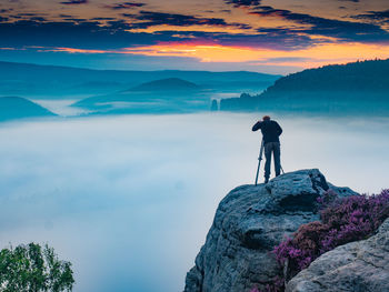 Skilled man photographing against misty landscape and morning sky. landscape photographer in action