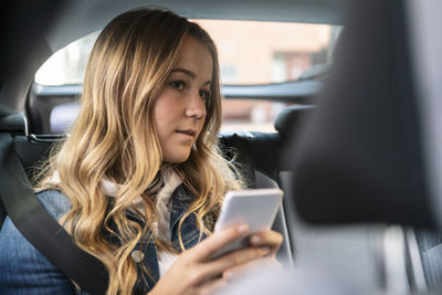 Female teenager using phone while sitting in car