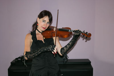 Portrait of beautiful woman playing violin against wall