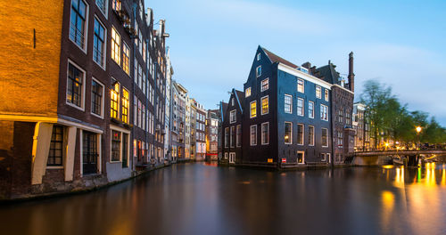 Canal amidst illuminated buildings in city against sky