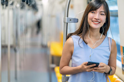 Portrait of smiling young woman using mobile phone while standing on bus