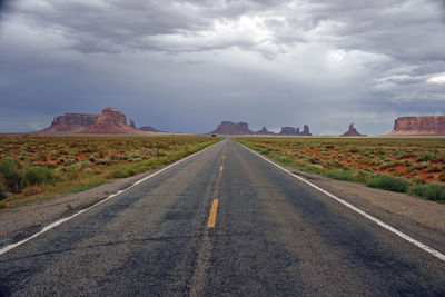 Road passing through field against cloudy sky