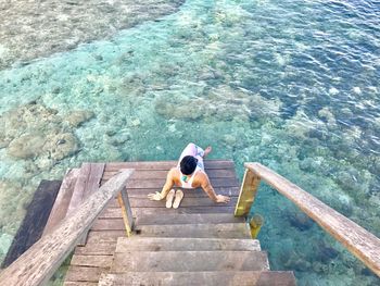 High angle view of man sitting on wooden planks by sea